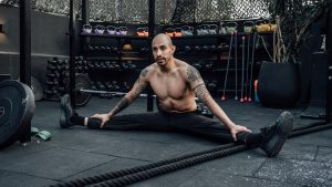 Tattooed man performing a split stretch in a gym, showcasing flexibility and fitness lifestyle in Mexico City.
